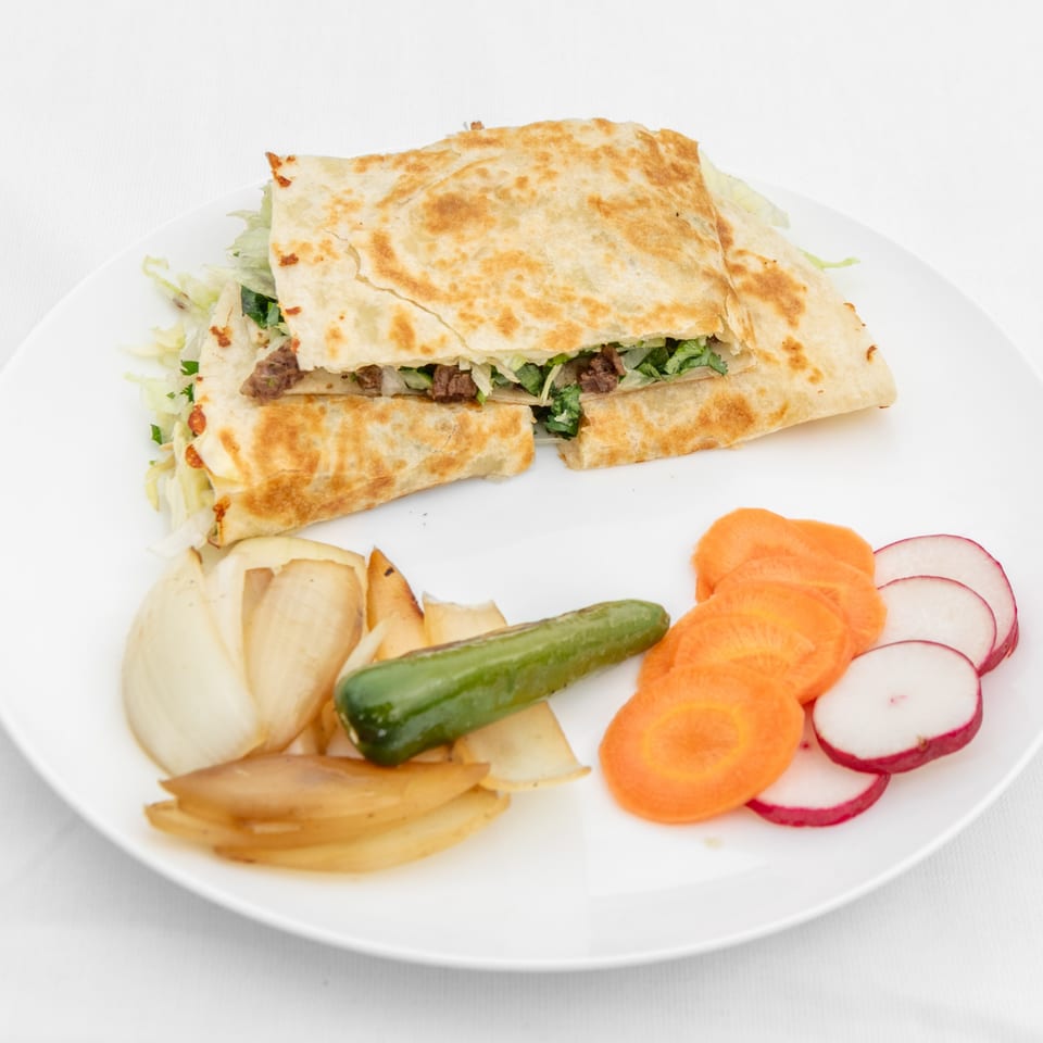 Taqueria El Jarocho Express quesadilla with meat, lettuce, and cilantro, served with grilled onions, jalapeño, carrots, and radishes.