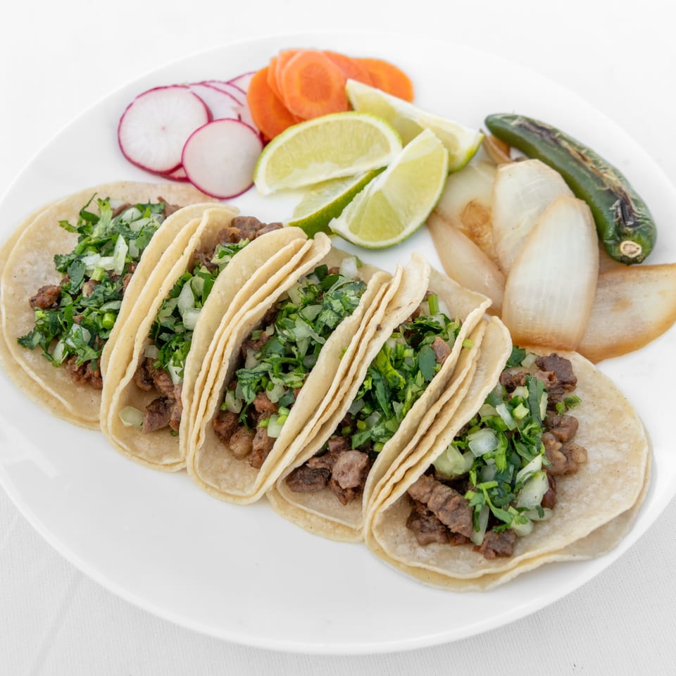 Five carne asada tacos with cilantro and onions, served with radishes, carrots, limes, grilled onions, and jalapeño.
