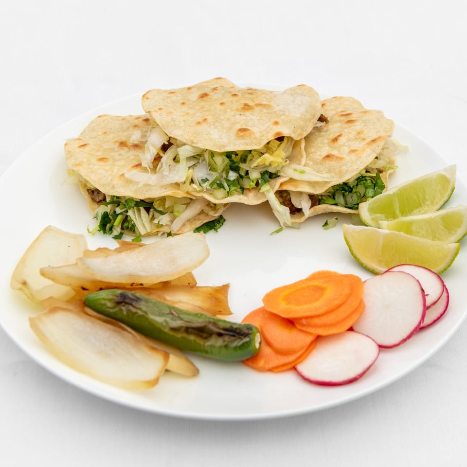 Three Taqueria El Jarocho Express tacos with lettuce, lime wedges, grilled pepper, and sliced vegetables.