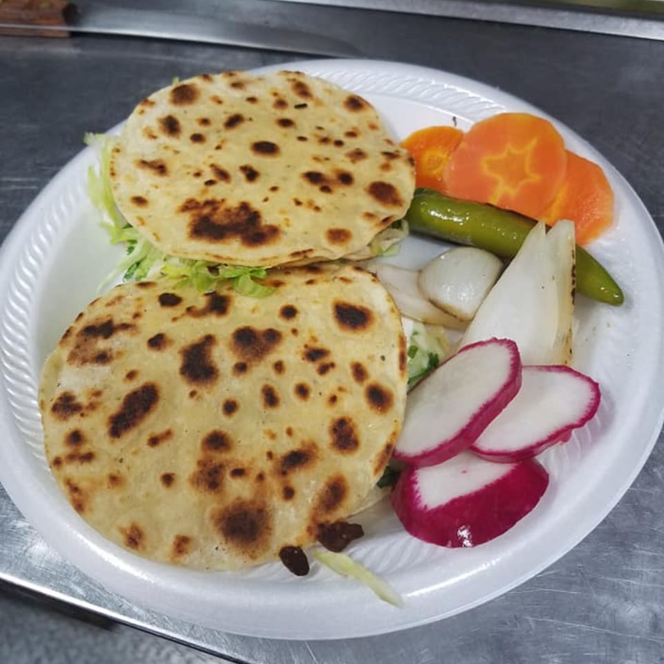 Two Mexican gorditas with lettuce, radishes, carrots, grilled onions, and a green chili on a plate.