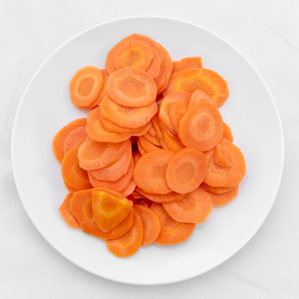A white plate filled with thinly sliced, bright orange carrots, ready to be served.