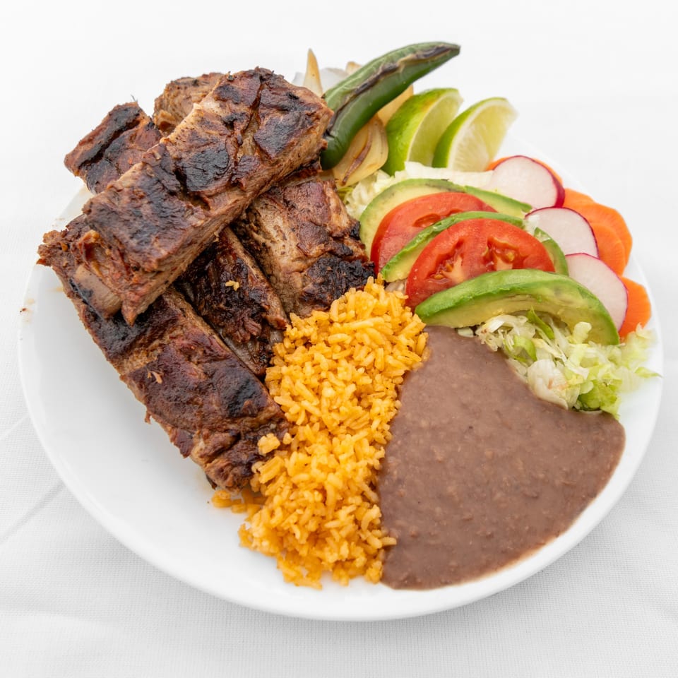 Grilled ribs with Mexican rice, refried beans, and a fresh salad with avocado, tomato, and radish.