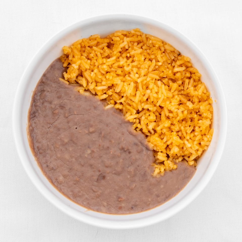 A white bowl filled with Mexican rice and refried beans, split down the middle.